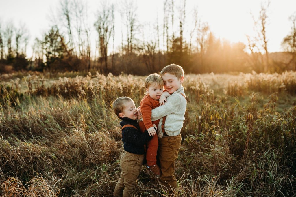 three boys hug in a field at sunset in November 2019