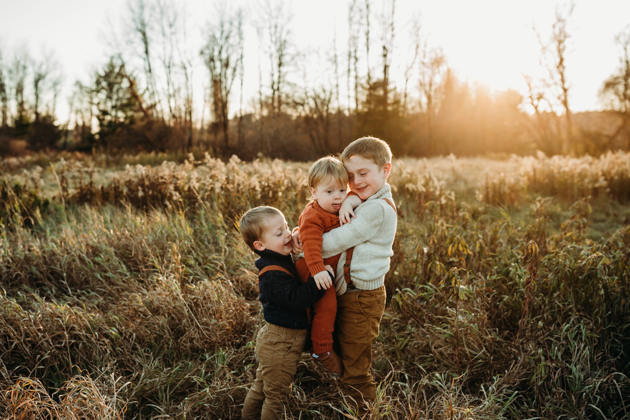 three boys hug in a field at sunset