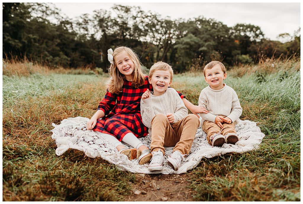 three-kids-sitting-on-lace-blanket-outdoors-belmont-family-photographer