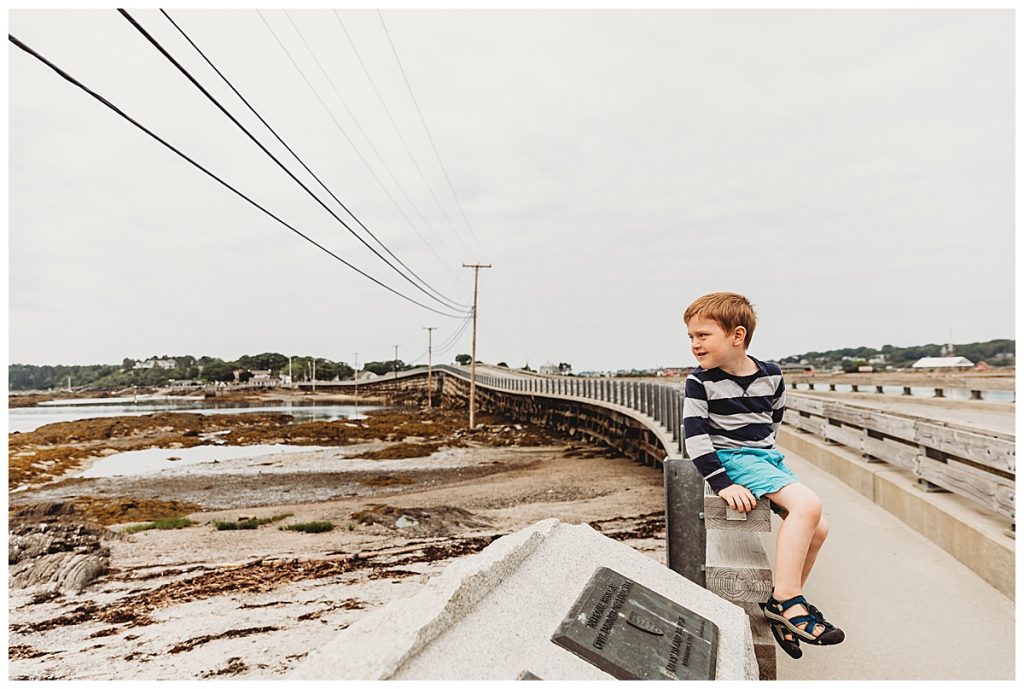 boy-sitting-on-bridge-railing-over-ocean-harbor