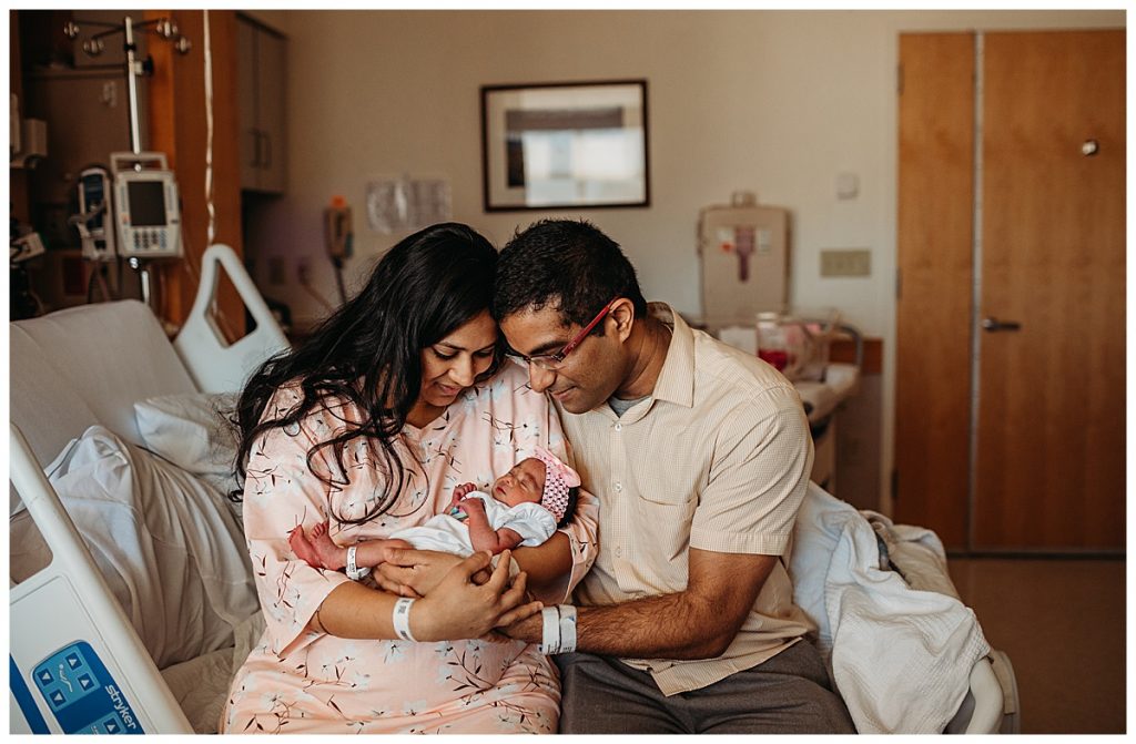 parents-holding-baby-girl-on-hospital-bed-newborn-photographer-in-boston