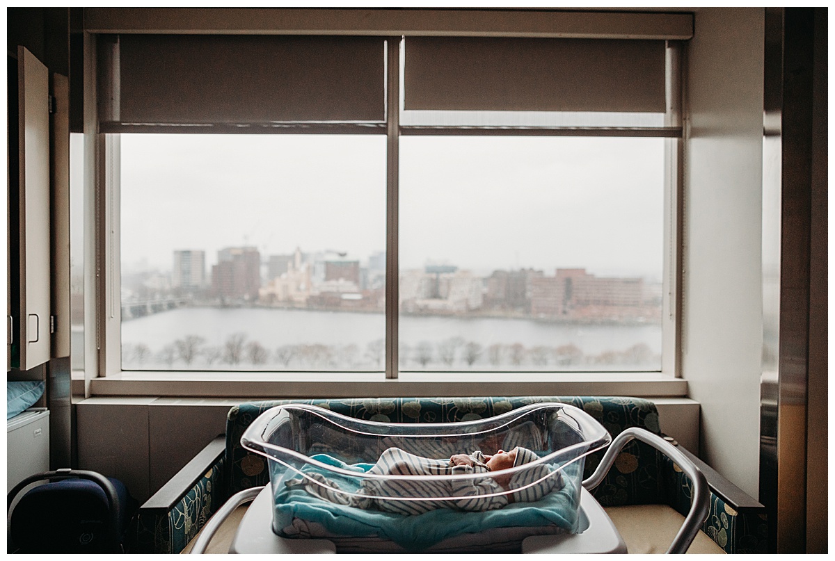 baby laying in hospital crib with a boston skyline view