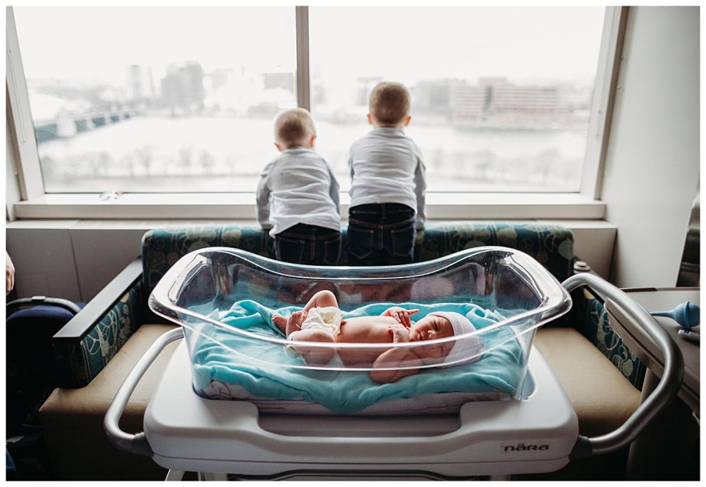 brothers looking out window while newborn yawns