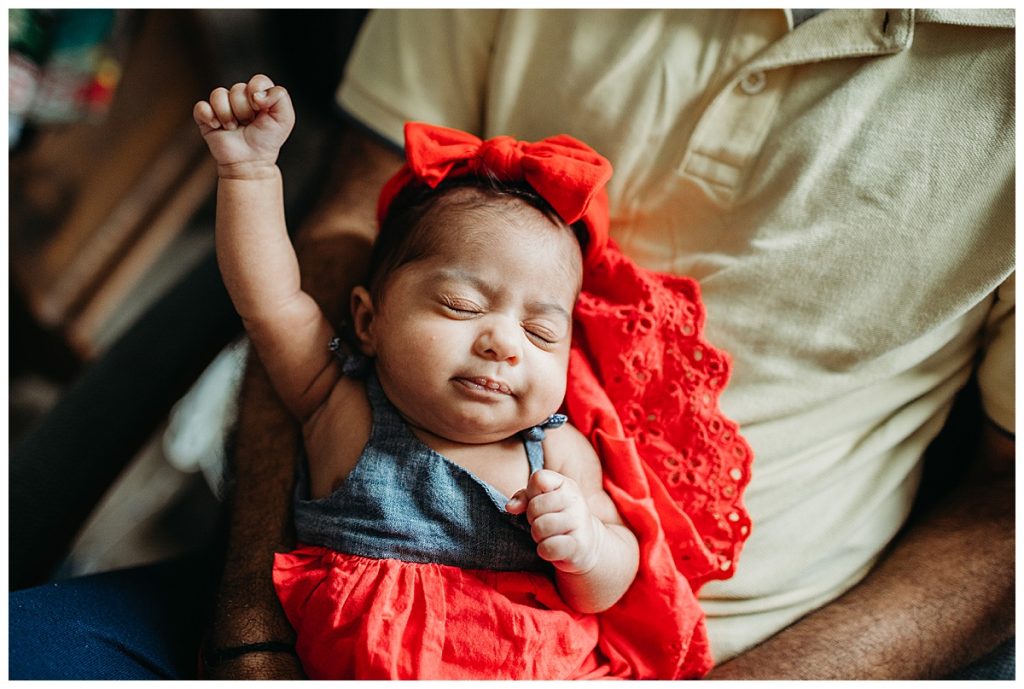 baby girl in red dress stretching while asleep during newborn photo session