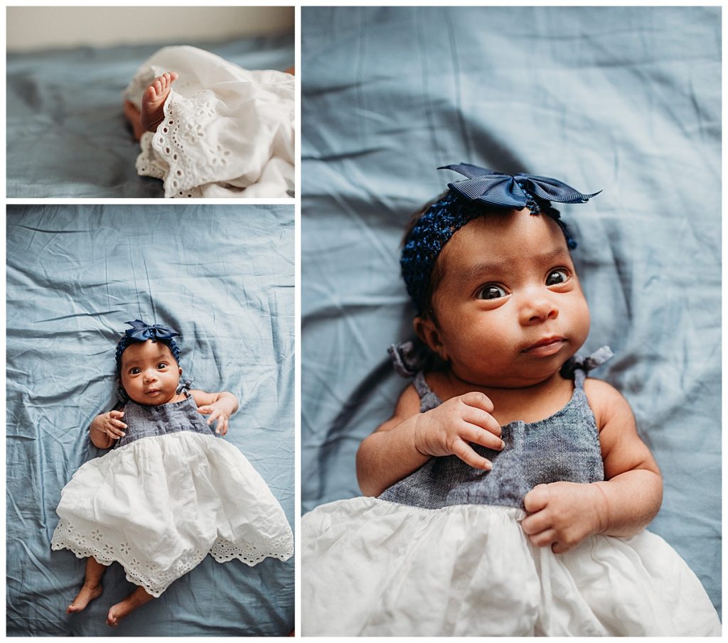 baby girl with denim dress and blue headband laying on blue bed sheets