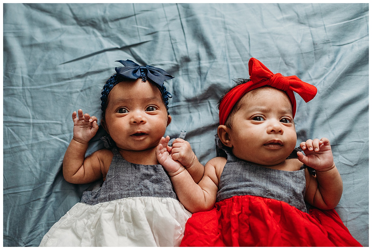 twin newborn girl laying on bed in matching dresses