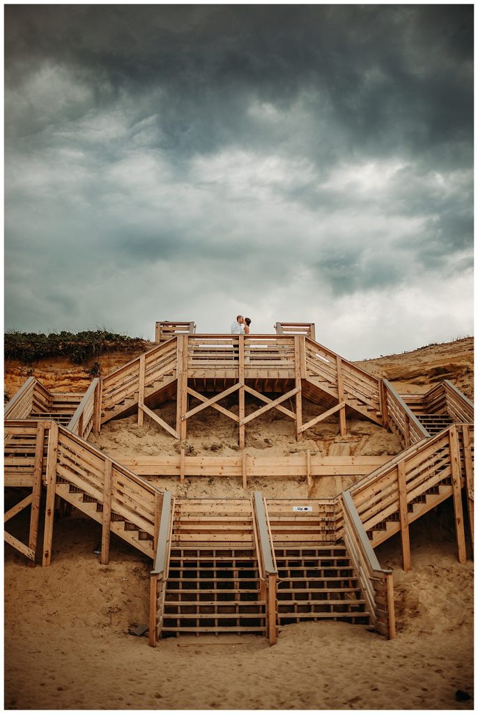 bride and groom stand under stormy skies atop a wooden beach staircase