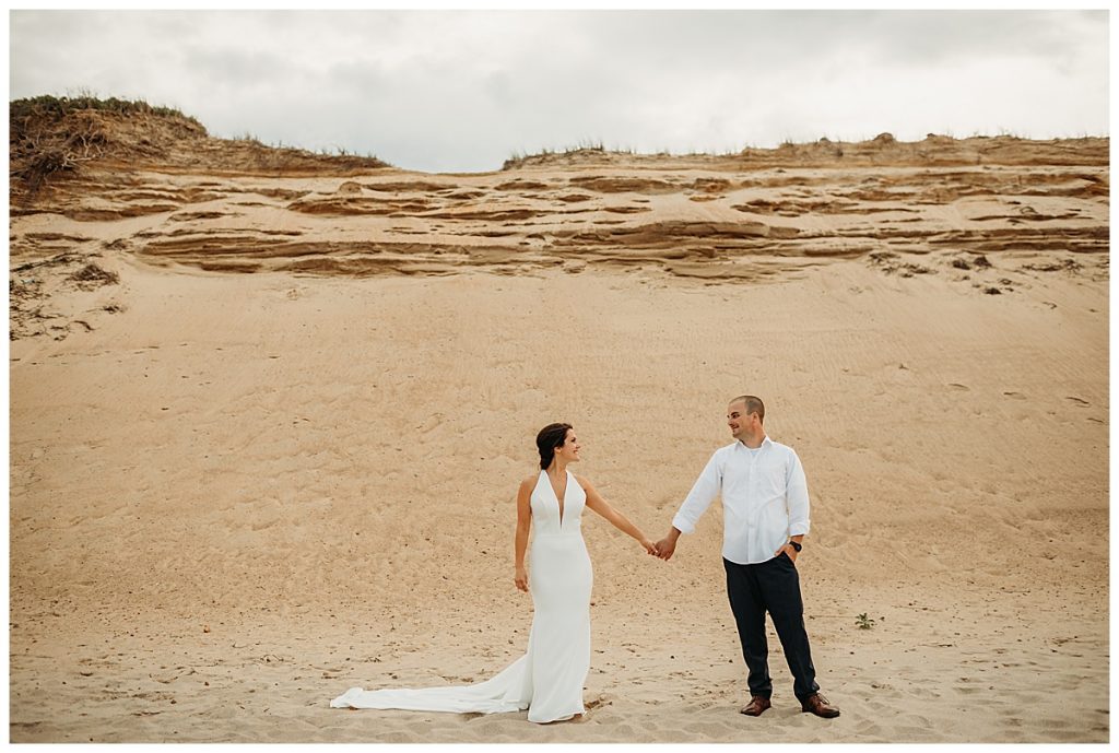 wedding couple holds hands on a sandy beach during ceremony