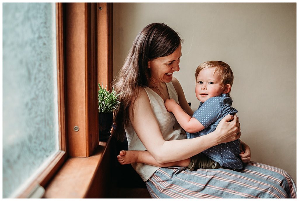 mother holds son lap on window seat during at-home family photography session