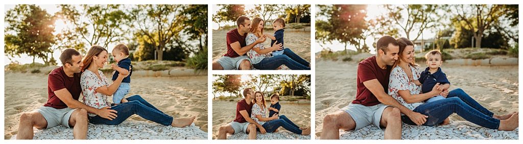 family sits in the sand at sunset with their one year old