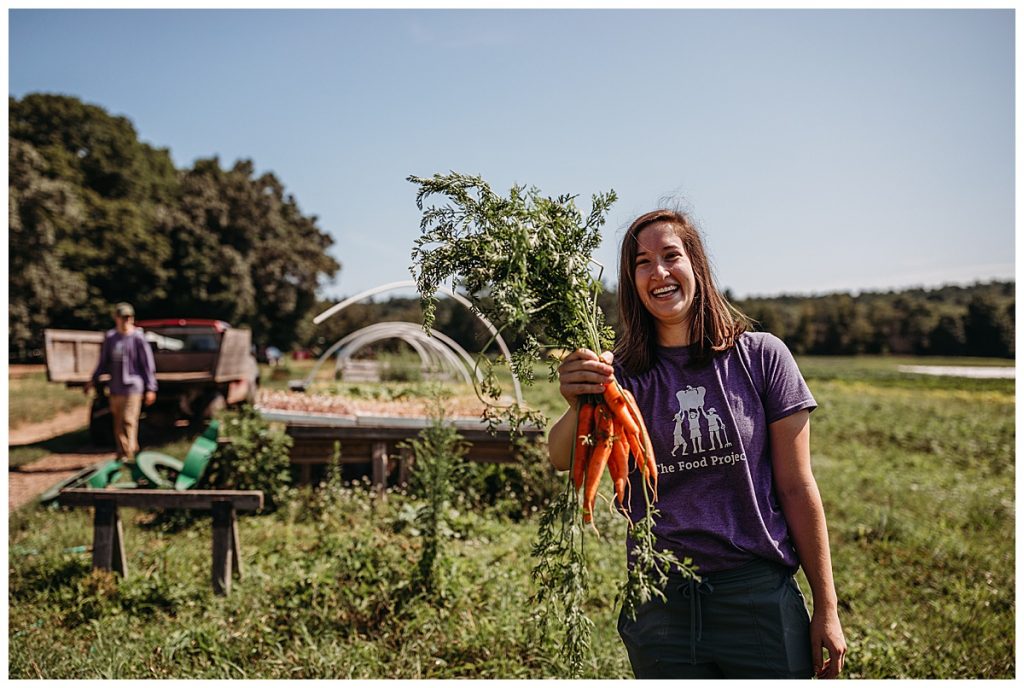 woman holds out a bunch of carrots on a farm