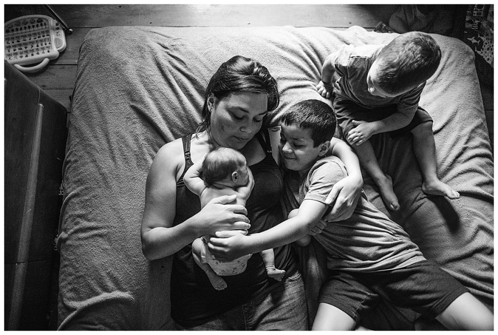 moody newborn photography with three kids on bed