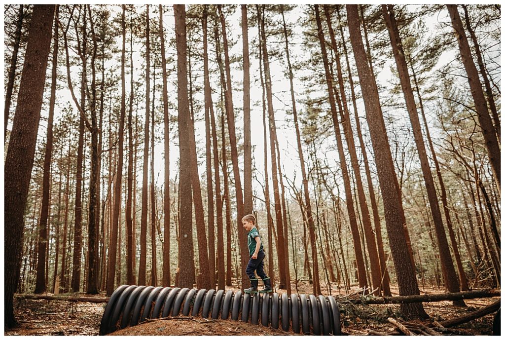 photo of a young boy climbing on a tube in the forest