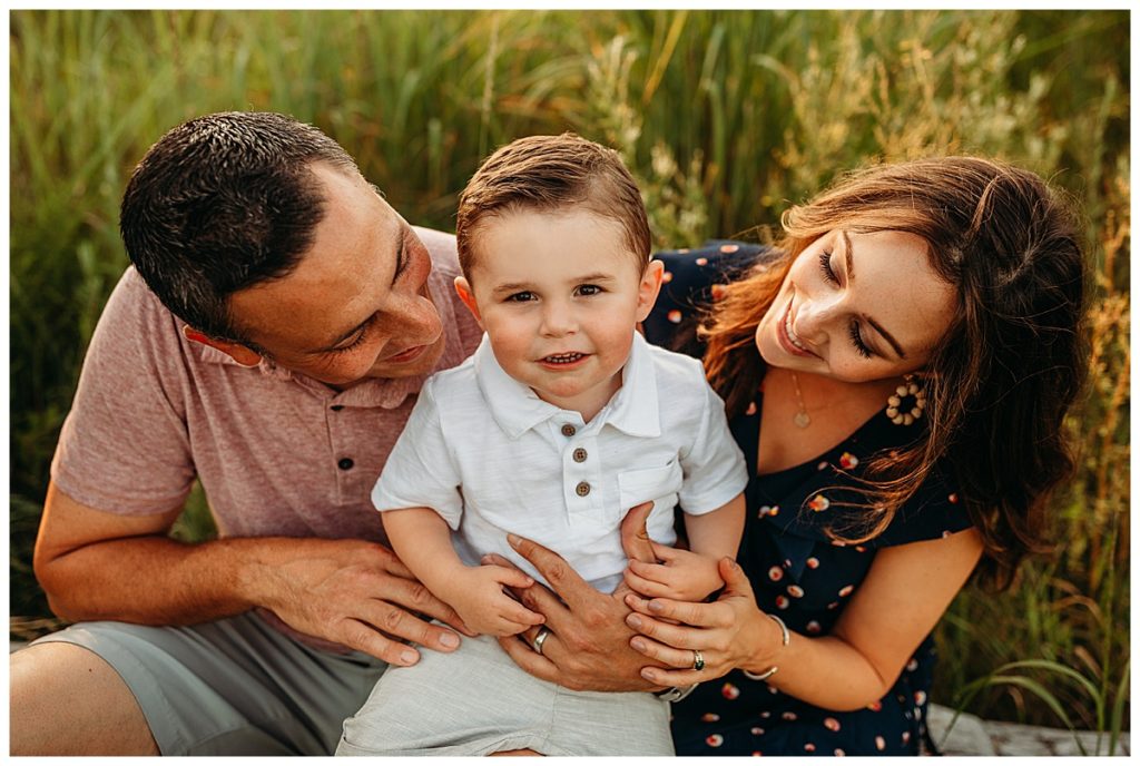 debunking family photography myths : two year old boy looks up at camera while parents snuggle him during family session