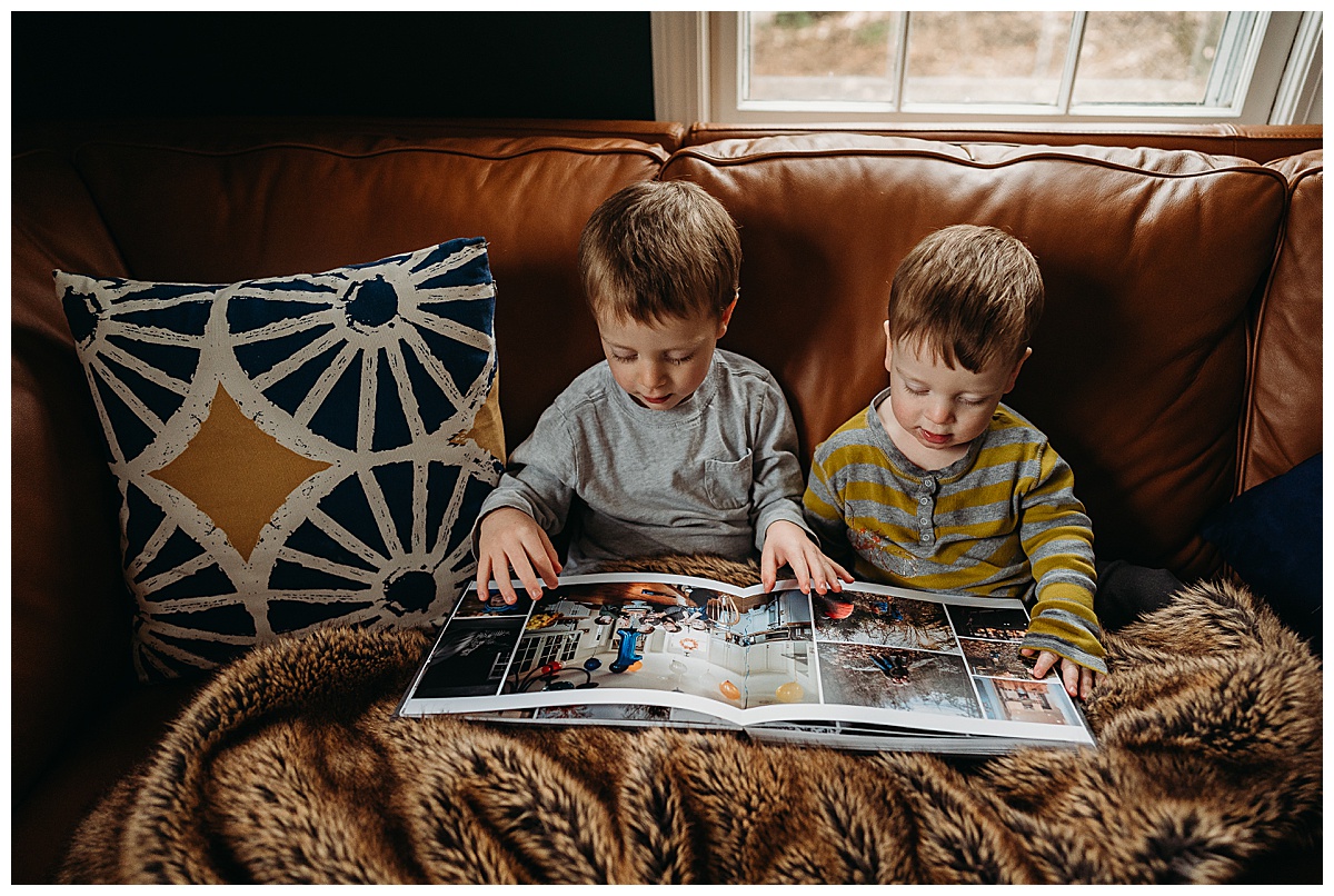 two boys look at family album under furry blanket on couch
