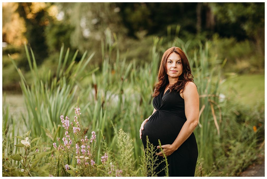 woman stands outdoors in reeds for maternity photoshoot in summer