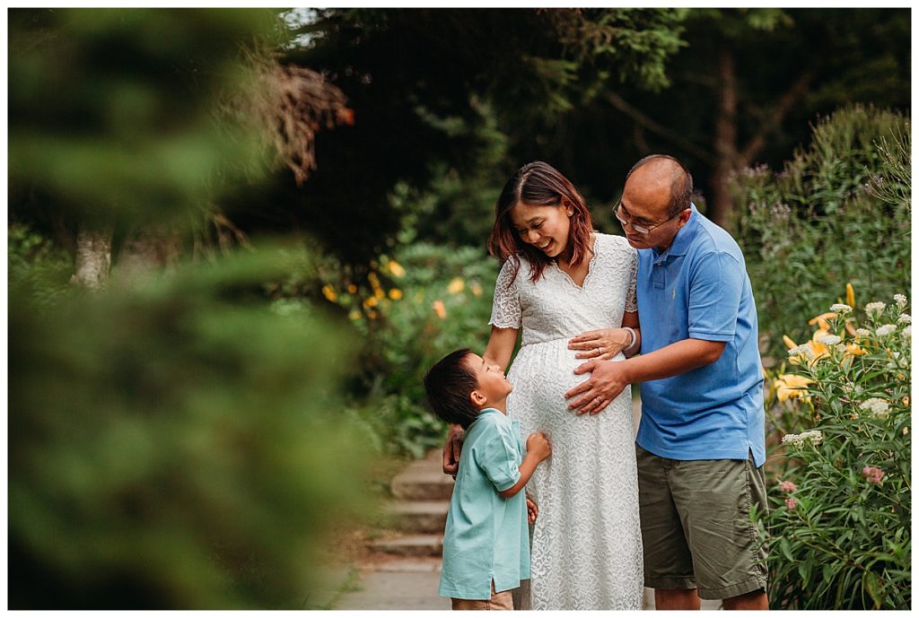 father and son touch moms pregnant belly in a garden durning maternity session in boston