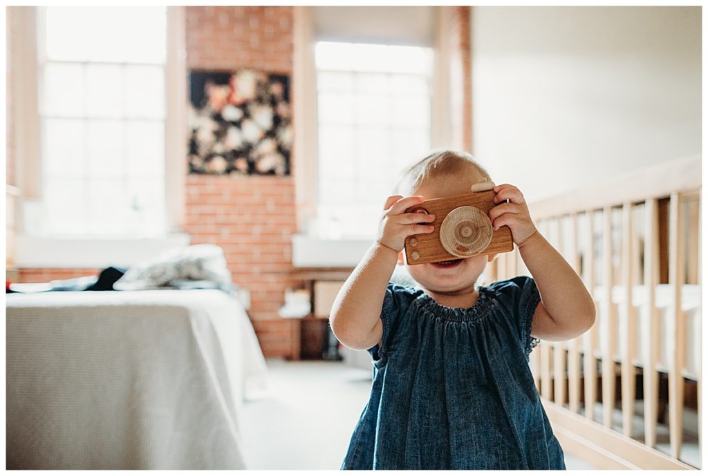 toddler girl holds wooden camera during newborn session
