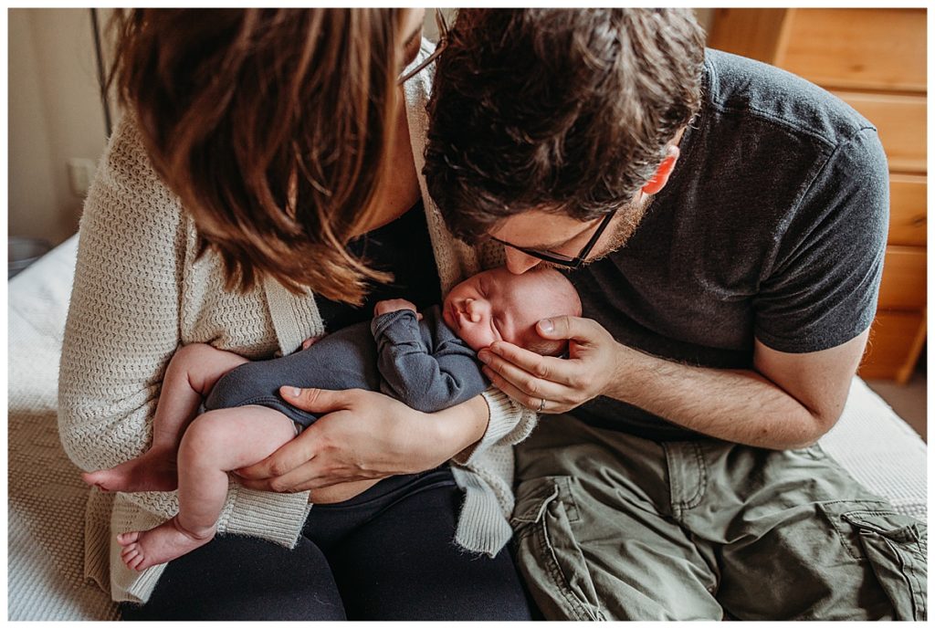 new parents kiss newborn baby boy on the head during in-home framingham newborn photography shoot