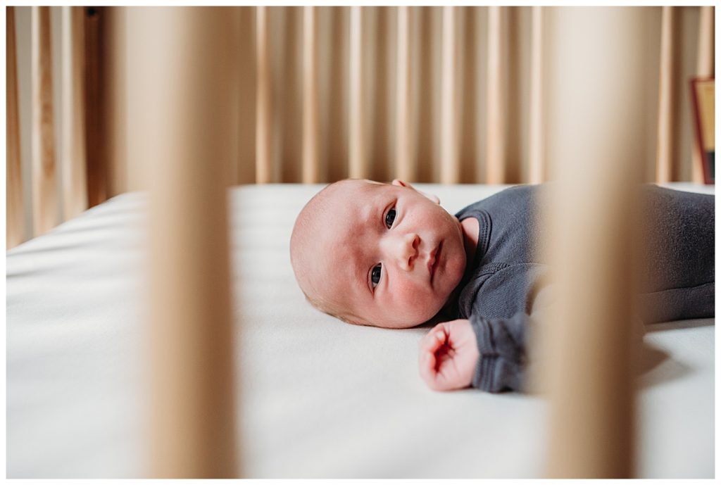 baby boy stares out of crib slats during his photoshoot