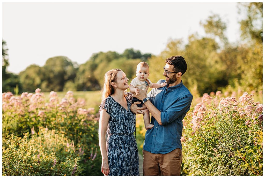 family of three standing in field of flowers