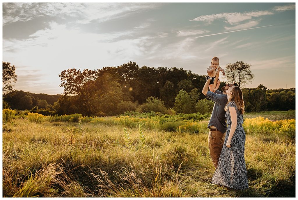 family lifts child in the air at sunset in a field during photoshoot