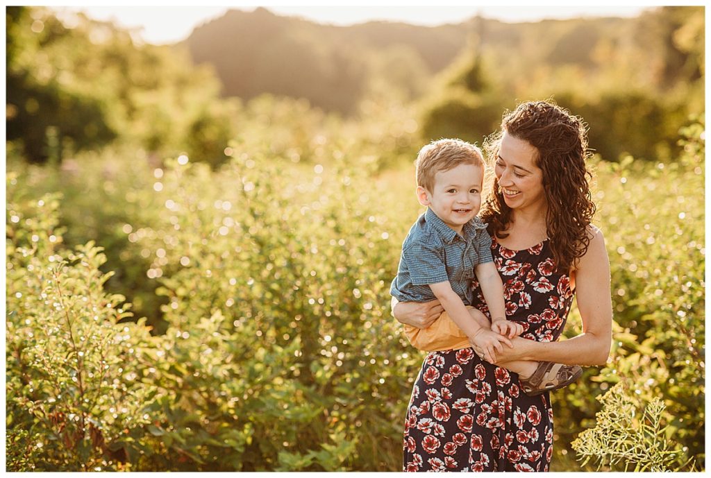 mom holds toddler boy in field and laughs