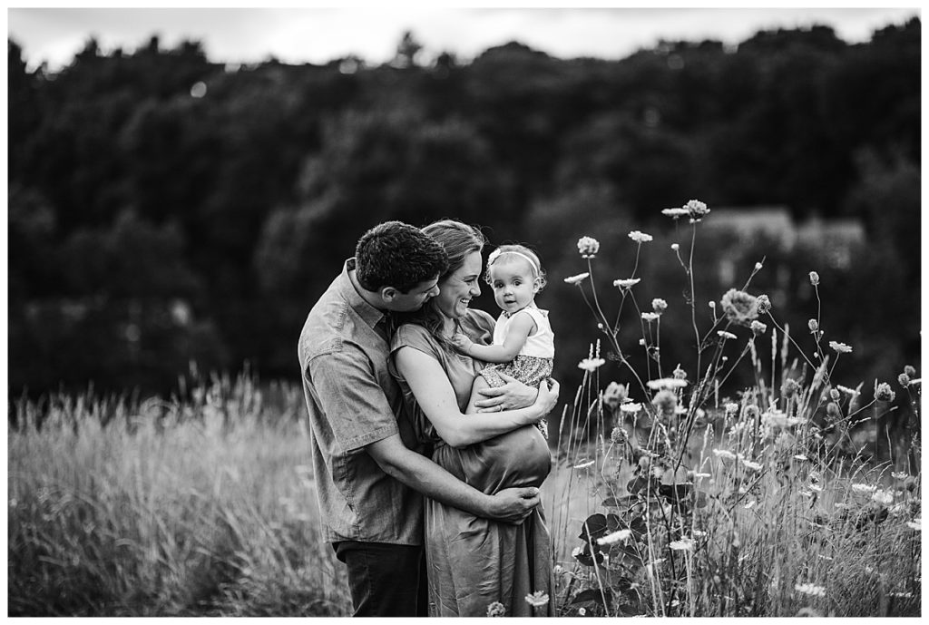 black and white portrait of pregnant mother and father with toddler in field of flowers