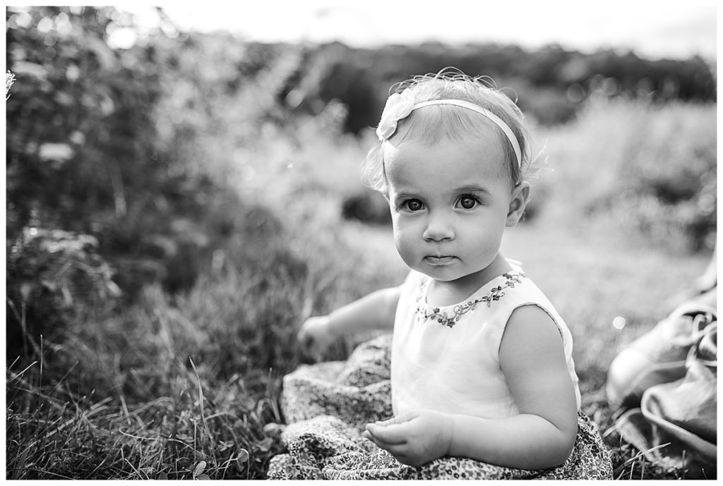 black and white image of toddler girl staring at camera in field