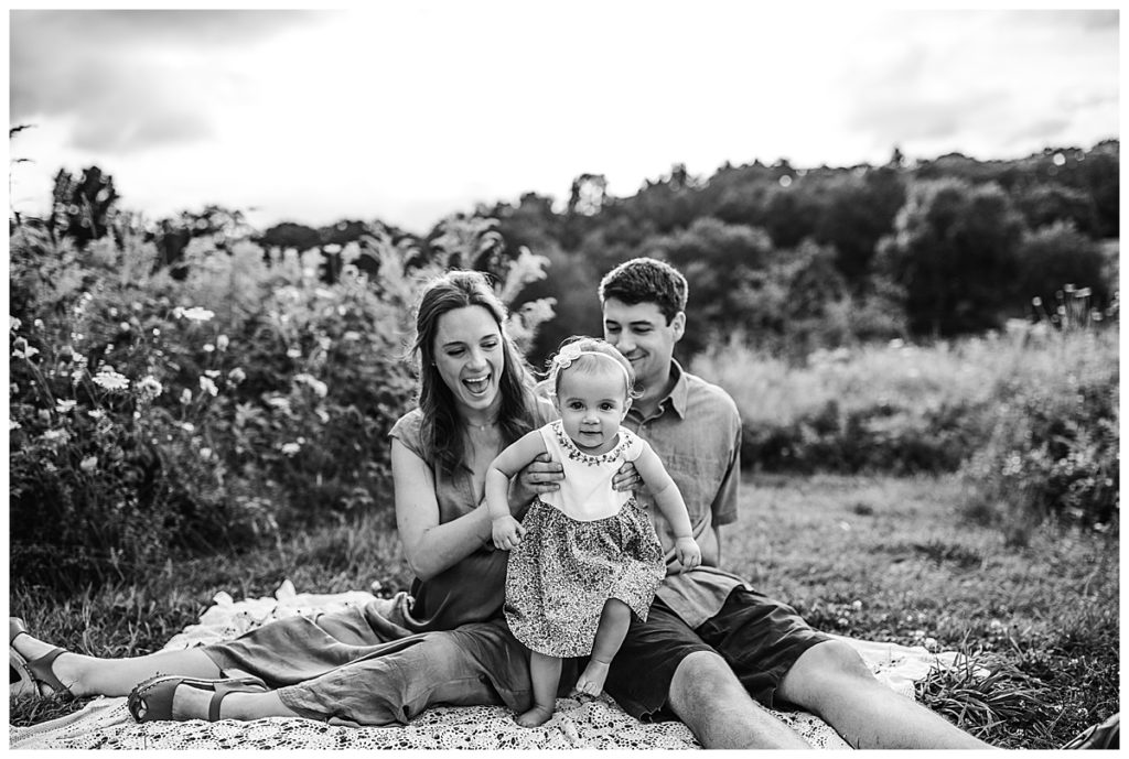 family of three sit on lace blanket in a field for repeat client photo example