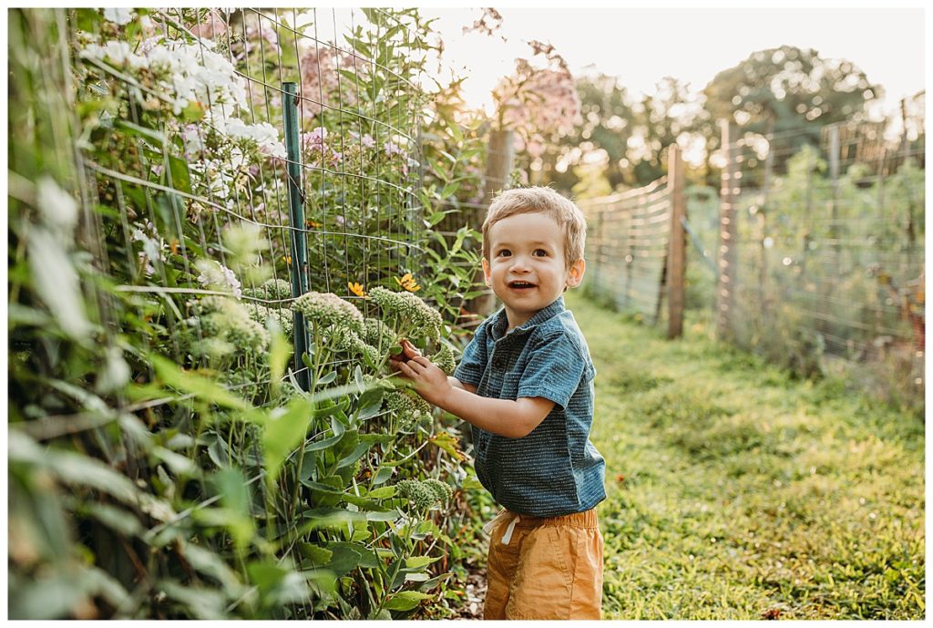 little boy in lush garden smiles at camera