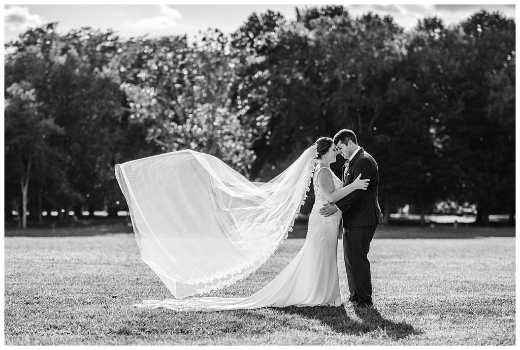 bride and groom in field with veil flying