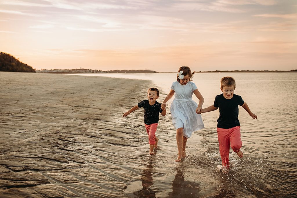 three kids run across a beach at sunset outside of boston