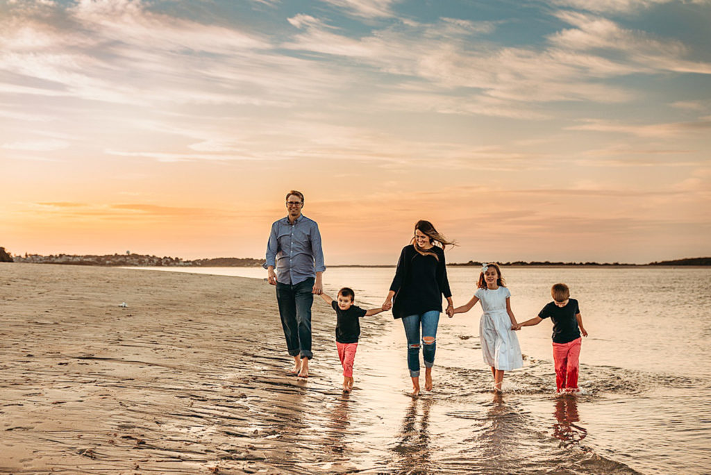 family of five holds hands and walks on beach during family photographer session in boston