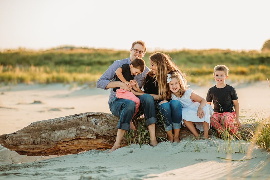 family sits on log at sunset during beach photoshoot
