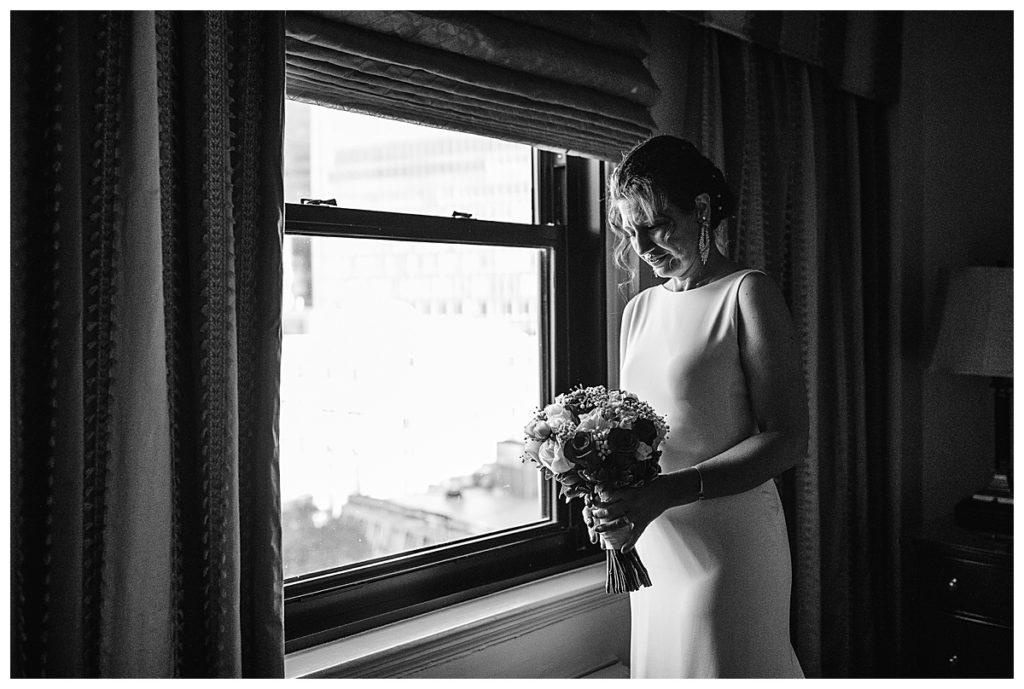 bride stands by window clutching bouquet for boston elopement