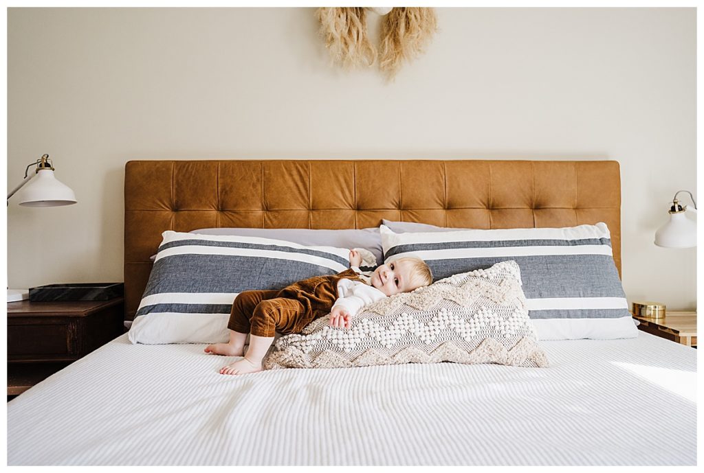 toddler lays on pillows on master bed during photo session
