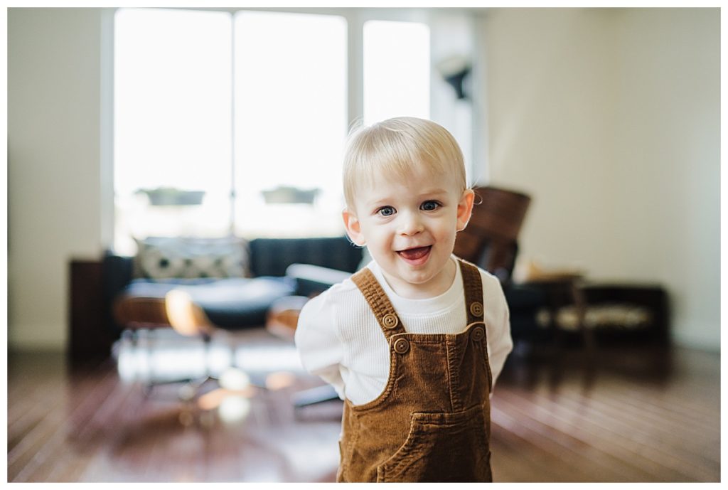 toddler boy in overalls smiles at camera