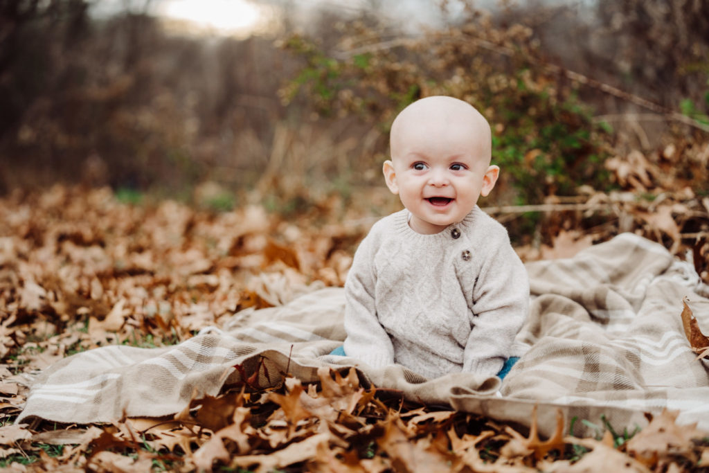 bald baby sits in November fall leaves for his family session