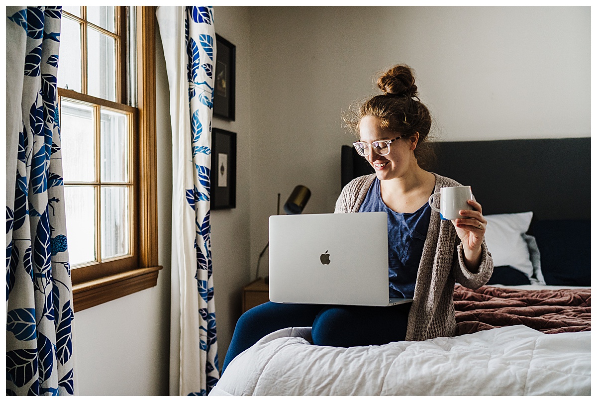 boston family photographer sits on bed with laptop and coffee