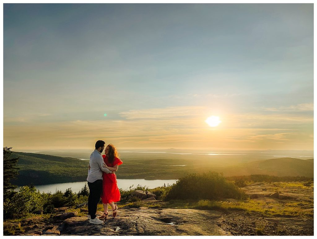couple embraces at sunset on top of Cadillac Mountain in Acadia National Park