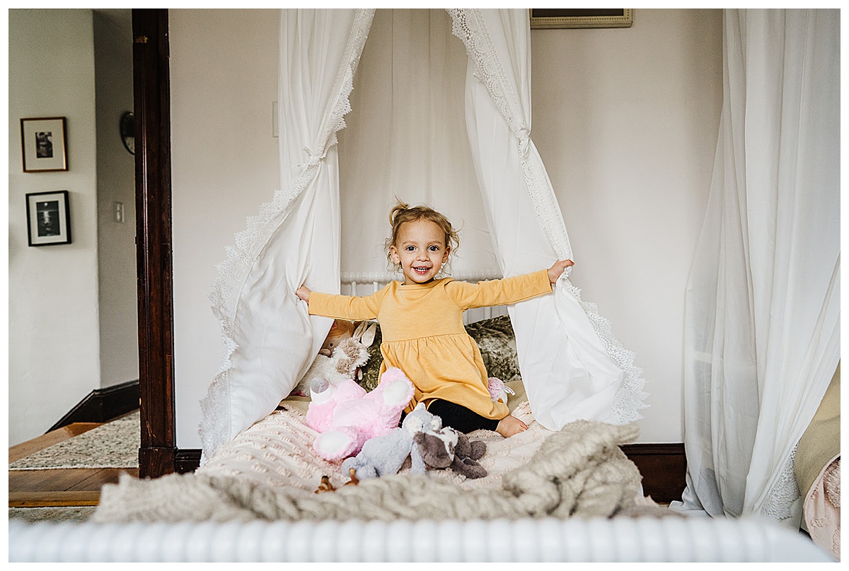 girl opens the curtains of her bed and laughs during family photoshoot
