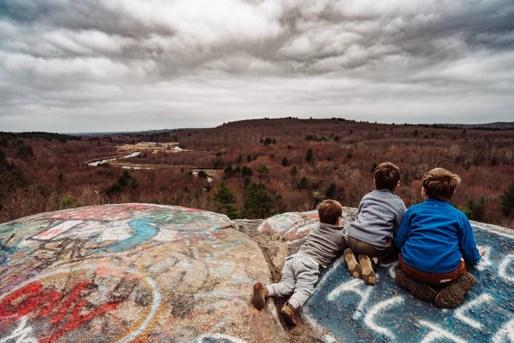 three boys look over the edge of a rock covered in graffiti