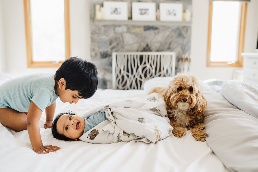 toddler boy peeks at baby brother on bed during boston newborn photographer photos